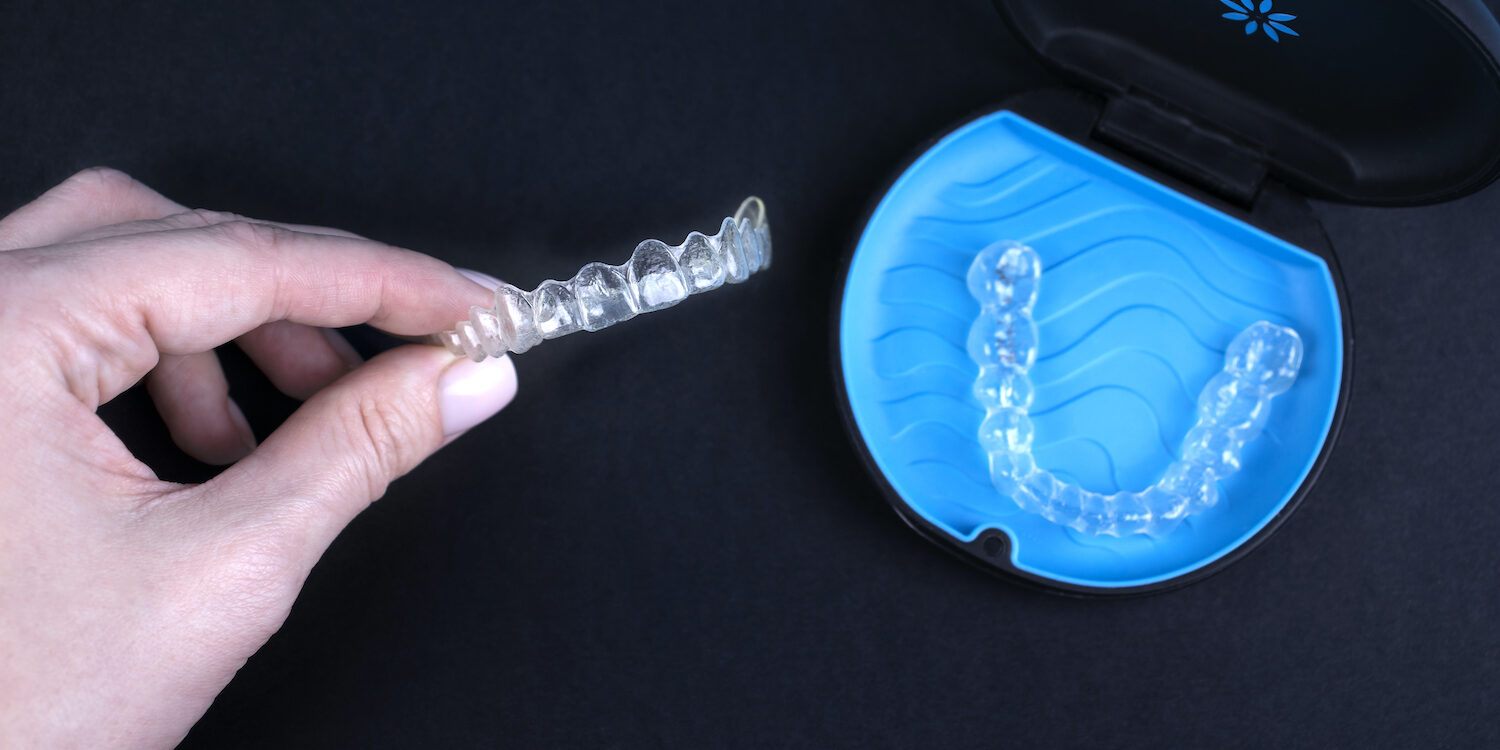 Woman holding invisible transparent aligners invisalign or plastic orthodontic braces. Black package with a box, clear-plastic retainers