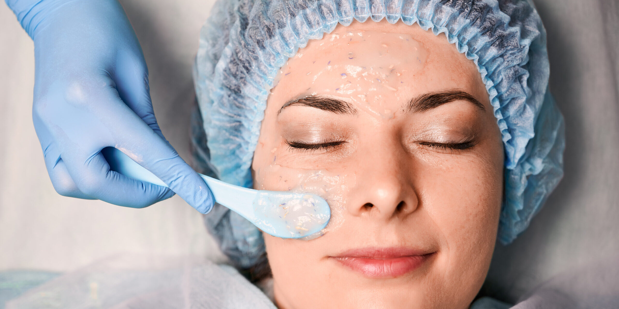 Cokaliteroi dermatologoi athinasmetologist hand applying cosmetic mask on woman face. kaliteroi dermatologoi athina